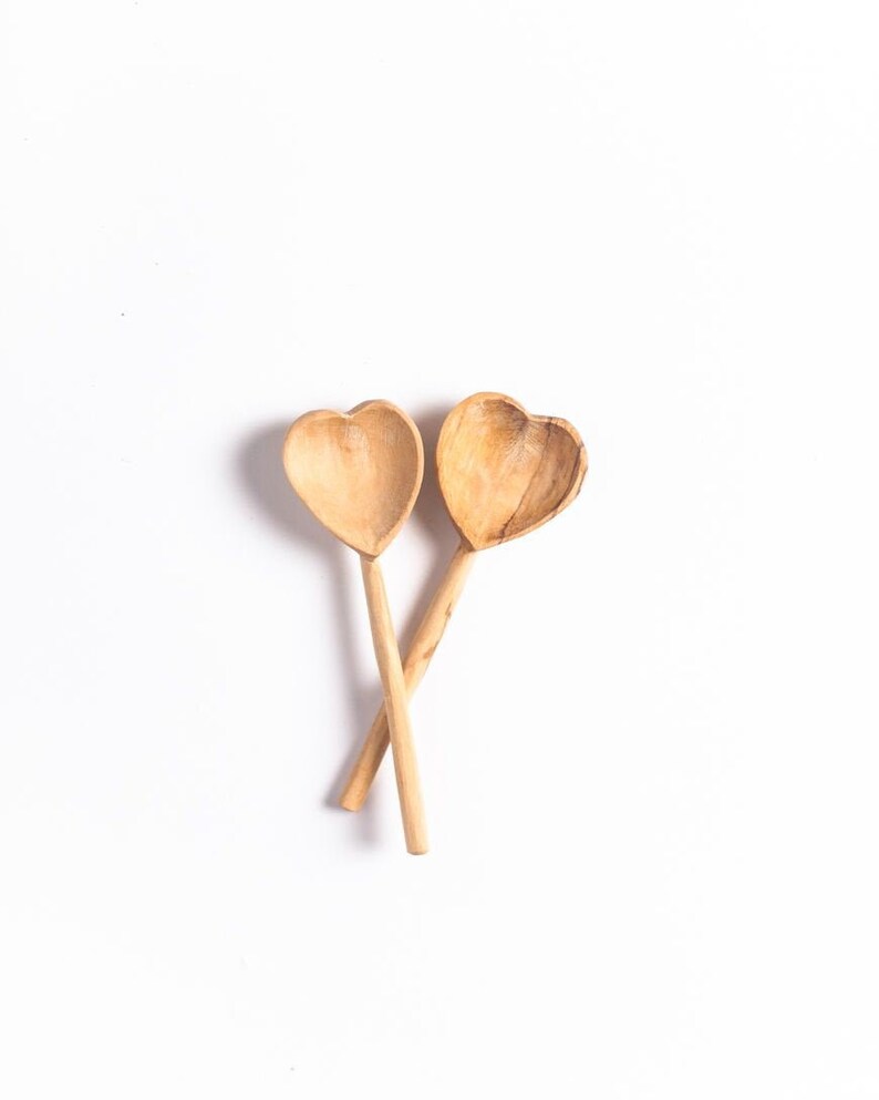 May include: Two wooden spoons shaped like hearts, crossed over each other. The spoons are made of light brown wood and have a natural finish.