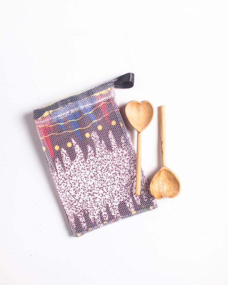 May include: Two wooden spoons with heart-shaped bowls, a black drawstring bag with a colorful patterned design, and a white background.