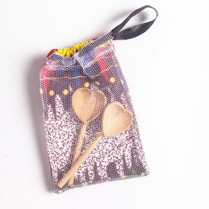 May include: A set of two wooden heart-shaped spoons in a mesh bag with a black drawstring. The bag has a colorful patterned design.