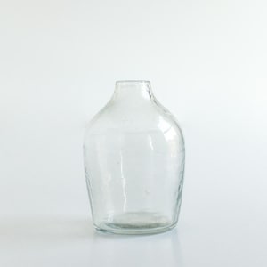 May include: A clear glass vase with a textured surface. The vase has a round body and a narrow opening.