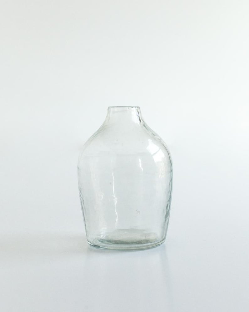 May include: A clear glass vase with a textured surface. The vase has a round body and a narrow opening.