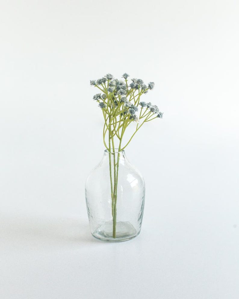 May include: A clear glass vase with a textured surface holds a bouquet of light blue flowers with green stems.