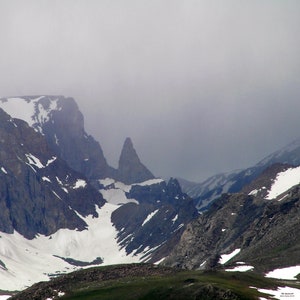 May include: A view of a mountain range with snow-capped peaks and a rocky outcropping in the distance. The mountains are shrouded in fog or clouds.