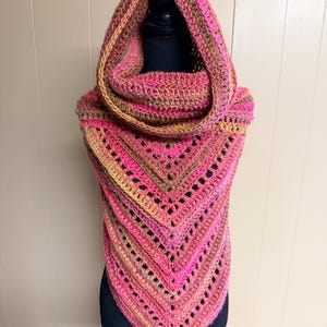 May include: A handmade crochet cowl and hood in shades of pink, brown, and yellow. The cowl features a triangular design with openwork details. The hood is attached to the cowl, creating a warm and stylish accessory.