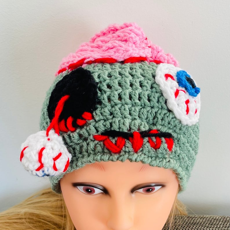 May include: Green, pink, white and black crocheted hat with stitched details and a stitched eye design.