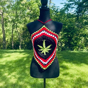 May include: A black crochet halter top with a green marijuana leaf design. The top is trimmed with red, white, and green yarn.