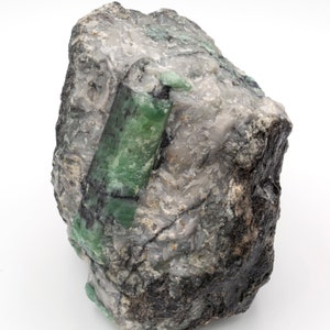 Può includere: Un grande masso grigio e ruvido con un grande cristallo di smeraldo verde incastonato.