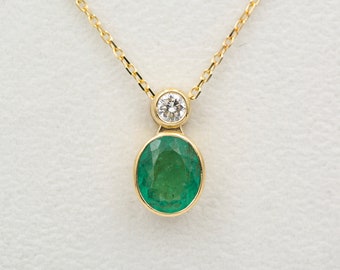 May include: A gold chain necklace with a pendant featuring a large oval emerald gemstone and a smaller round diamond.