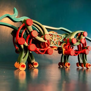 May include: A teal blue and red wooden toy animal with wheels. The toy is a stylized cow with a complex gear system.