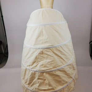 May include: A white, multi-layered petticoat with a circular shape. The petticoat is made of a soft, lightweight fabric and has a smooth, even texture. It is designed to create a full, flowing silhouette.