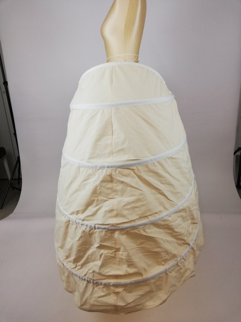 May include: A white, multi-layered petticoat with a circular shape. The petticoat is made of a soft, lightweight fabric and has a smooth, even texture. It is designed to create a full, flowing silhouette.
