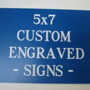May include: A rectangular blue sign with white text that reads 5x7 CUSTOM ENGRAVED SIGNS. The sign features a bold, centered font and a clean, flat surface design, providing a clear visual representation of the product's text and color scheme.