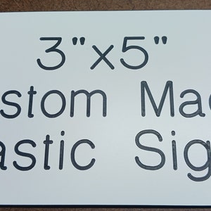 May include: White plastic sign with black text that reads "3" x 5" Custom Made Plastic Signs".