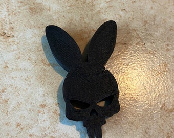 May include: Black bunny skull-shaped decorative item. The design combines a bunny silhouette with a skull, featuring long ears and eye sockets. The item is made of a solid black material and is likely a decorative piece.