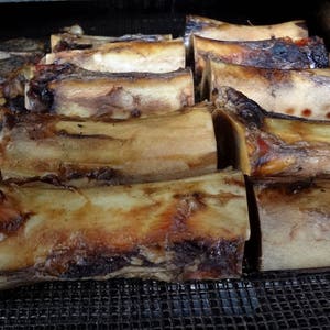 May include: A close-up shot of roasted beef bones, displaying a range of sizes and shapes. The bones have a rich, golden-brown exterior with darker, charred patches. The image is taken from a slightly elevated angle, highlighting the texture and detail of the cooked bones.
