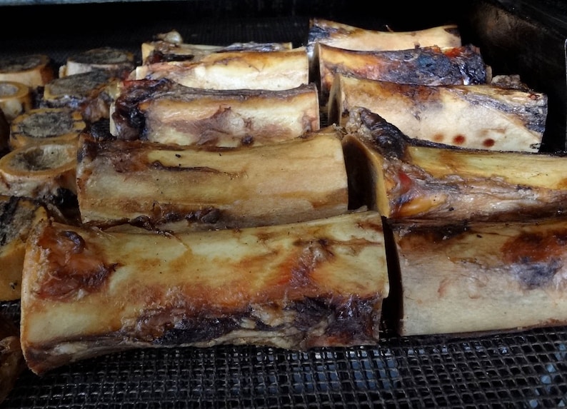 May include: A close-up shot of roasted beef bones, displaying a range of sizes and shapes. The bones have a rich, golden-brown exterior with darker, charred patches. The image is taken from a slightly elevated angle, highlighting the texture and detail of the cooked bones.