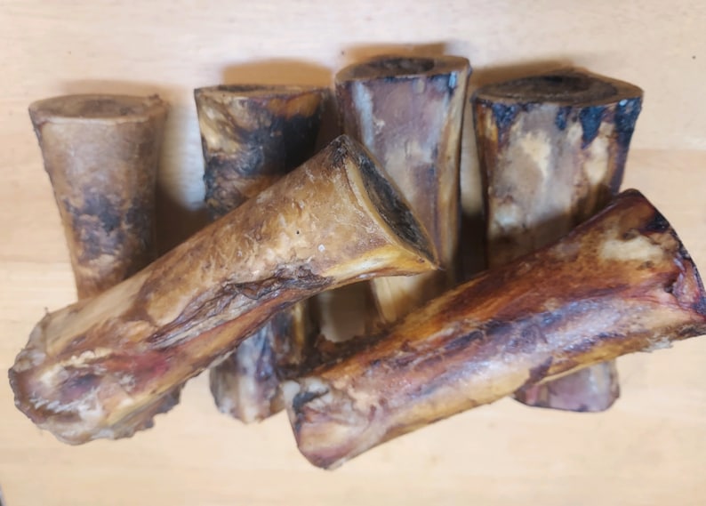 May include: A selection of beef marrow bones, presenting a natural, rustic appearance. The bones exhibit a spectrum of colours, from pale tan to dark brown, with visible textures and variations. The ends are cut, revealing the marrow cavity.