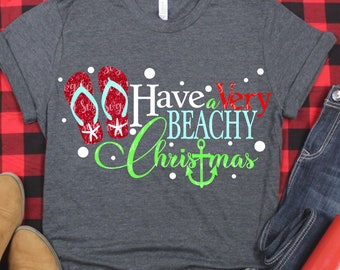 Könnte beinhalten: Ein graues T-Shirt mit dem Text "Have a Very Beachy Christmas" in grüner, roter und blauer Schrift. Das Design enthält auch ein Paar rote Flip-Flops mit weißen Schneeflocken und einem grünen Anker.