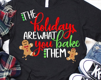 May include: A black t-shirt with the text "The holidays are what you bake them" in red, white, and green glitter. Two gingerbread cookies are on either side of the text.
