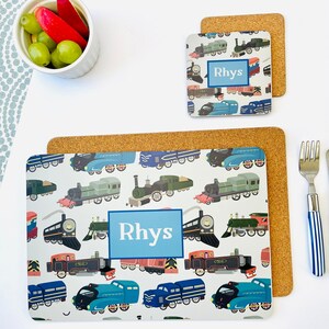 May include: A blue and white placemat with a repeating pattern of colourful trains. The placemat has the name "Rhys" printed in a blue box. The placemat is made of cork.