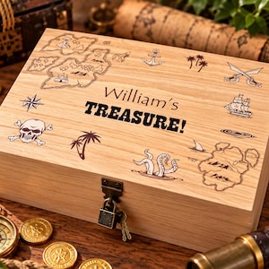 May include: A rectangular light-coloured wooden box with a hinged lid and a metal padlock. The lid features laser-engraved nautical illustrations including a map, skull, anchor, ship, and palm trees, with the text William's TREASURE! in the centre.