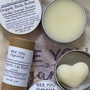 May include: Three different sizes of organic body care products from Bee You Organics. A small tin of organic body butter in vanilla orange dream, a larger tin of organic body bar in orange vanilla dream, and a tube of organic lip balm in vanilla. All products are labeled with the company name and website.