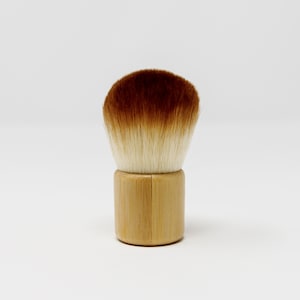 May include: A brown and white makeup brush with a wooden handle. The brush is made of natural bristles and is designed for applying powder or blush.