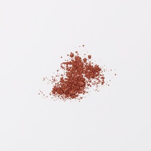 May include: A close-up of a pile of loose, reddish-brown eyeshadow powder on a white background.