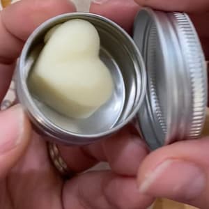 May include: A heart-shaped, white, solid balm in a silver tin with a lid.