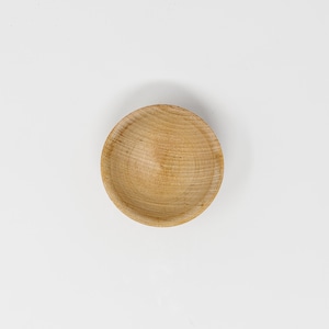 May include: A small, round wooden bowl with a natural wood finish. The bowl is empty and has a smooth, slightly textured surface.