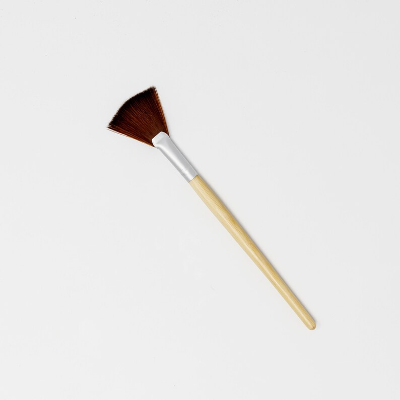 May include: A brown fan-shaped makeup brush with a wooden handle.