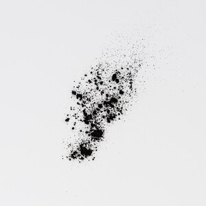 May include: Black powder scattered on a white background. The powder is in a loose, irregular shape, with some of it forming small clumps.