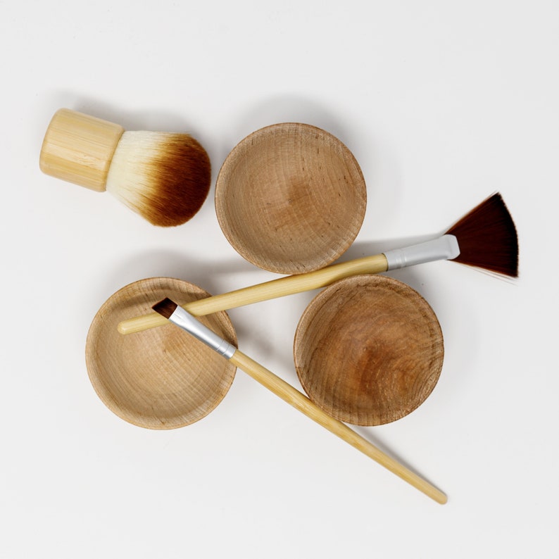 May include: Three wooden bowls and two makeup brushes. The bowls are light brown and have a natural wood grain. The brushes are made of natural bristles and have wooden handles.