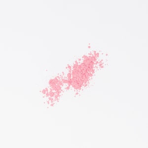May include: A pink powder blush makeup product scattered on a white background.