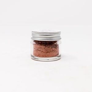 May include: A small glass jar with a silver lid filled with a light brown powder.