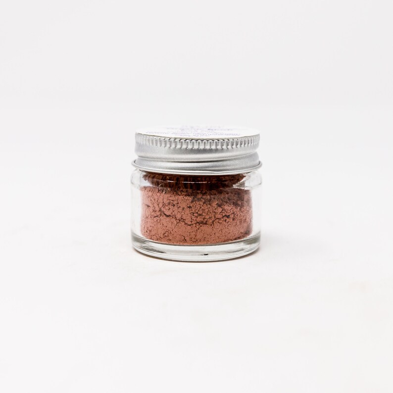 May include: A small glass jar with a silver lid filled with a light brown powder.