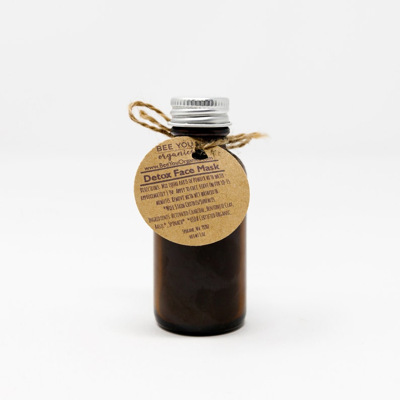 May include: A small brown glass bottle with a silver lid and a brown paper label that says "Bee You Organic" and "Detox Face Mask". The label also includes instructions for use and a list of ingredients, including activated charcoal, bentonite clay, basil, spinach, and other certified organic ingredients.