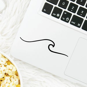 May include: A white laptop with a black keyboard and a black wave sticker on the top of the laptop. The laptop is on a white fluffy surface with a bowl of popcorn and a clear glass bottle with a pink lid and a pink straw.