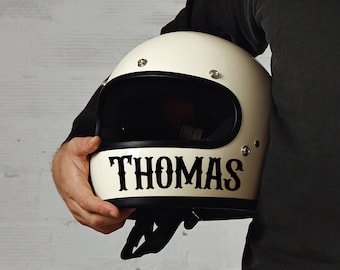 May include: A white motorcycle helmet with a black visor and the name "THOMAS" written in black letters on the front.