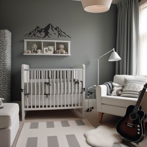 May include: A white crib with a gray and white patterned mattress, a white armchair with gray and white patterned pillows, a gray wall with a black mountain silhouette decal, and a white shelf with stuffed animals.