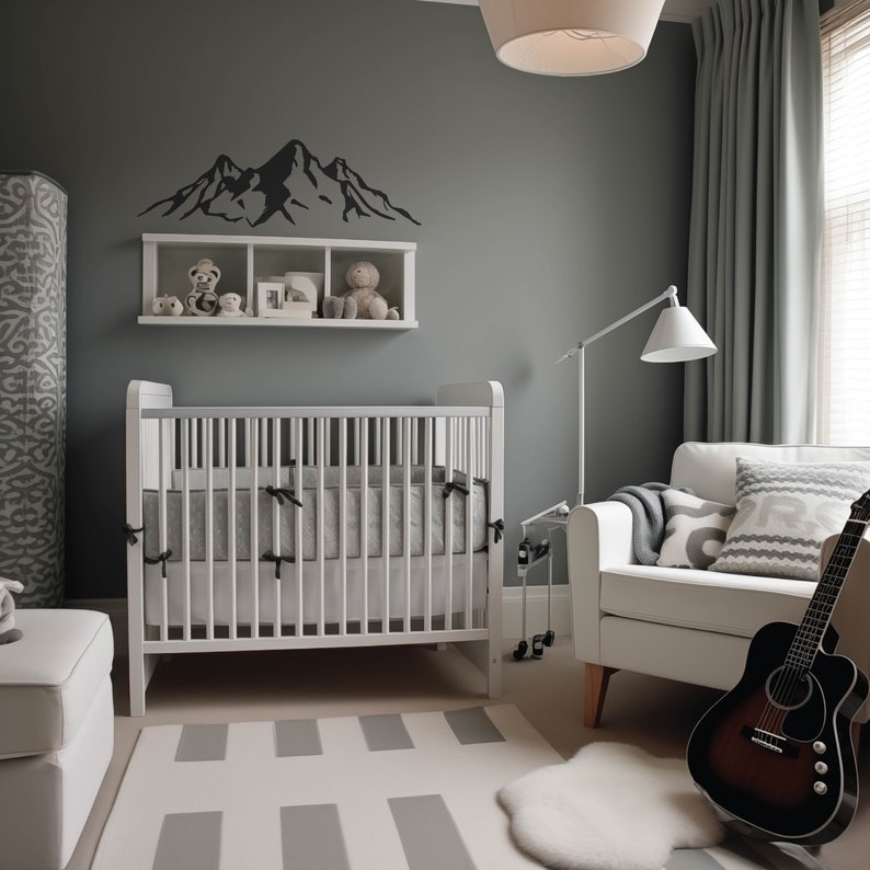 May include: A white crib with a gray and white patterned mattress, a white armchair with gray and white patterned pillows, a gray wall with a black mountain silhouette decal, and a white shelf with stuffed animals.