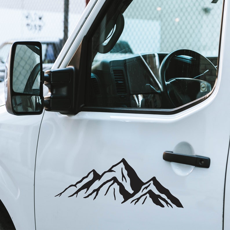 May include: A white van with a black mountain range decal on the side door. The decal is a simple silhouette of mountains with peaks and valleys.