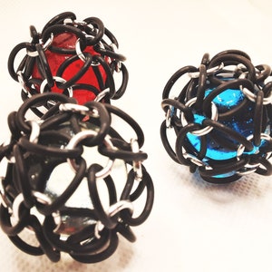 May include: Three glass marbles encased in black rubber mesh. The marbles are red, blue, and clear.