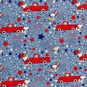 May include: A blue fabric with a repeating pattern of red pickup trucks, fireworks, stars, and Snoopy characters. Snoopy is wearing a red, white, and blue hat and is holding a flag.