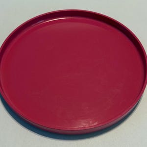 May include: A bright pink round plastic tray. The tray is smooth and has a slightly raised edge.