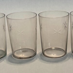 May include: Four clear drinking glasses with etched starburst designs. The glasses are cylindrical with a slightly tapered shape and a simple, elegant aesthetic. Perfect for serving water, juice, or cocktails.
