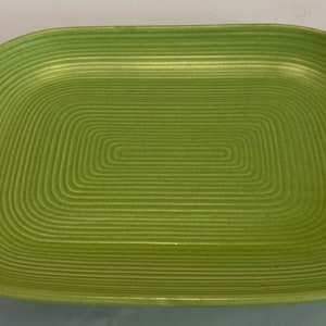 May include: A rectangular, lime green ceramic serving platter with rounded corners. The surface features a concentric, ridged pattern. The dish is suitable for serving appetizers or small dishes.