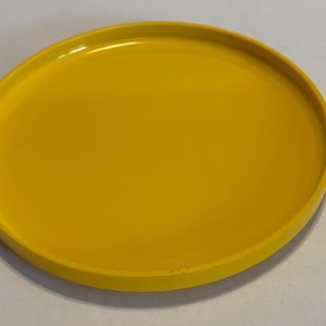 May include: A bright yellow, round plate with a slightly raised edge. The plate has a smooth, glossy finish and is set against a neutral background. The design is simple and modern, suitable for serving food or as a decorative item.