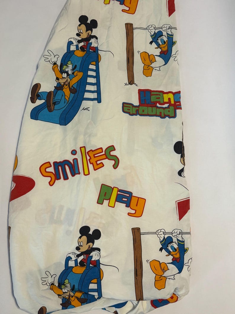 Puede incluir: S&aacute;bana bajera blanca con Mickey Mouse, Goofy y el Pato Donald en poses juguetonas. La s&aacute;bana tiene las palabras "Smiles", "Play" y "Hang Around" en letras coloridas. La s&aacute;bana est&aacute; dise&ntilde;ada con un tema de dibujos animados.