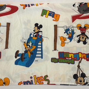 Puede incluir: S&aacute;bana blanca con un tema l&uacute;dico de Disney. Mickey Mouse, Goofy y el Pato Donald aparecen en ilustraciones coloridas. Tambi&eacute;n est&aacute;n presentes las palabras "Play", "Hanging Around" y "Smiles".